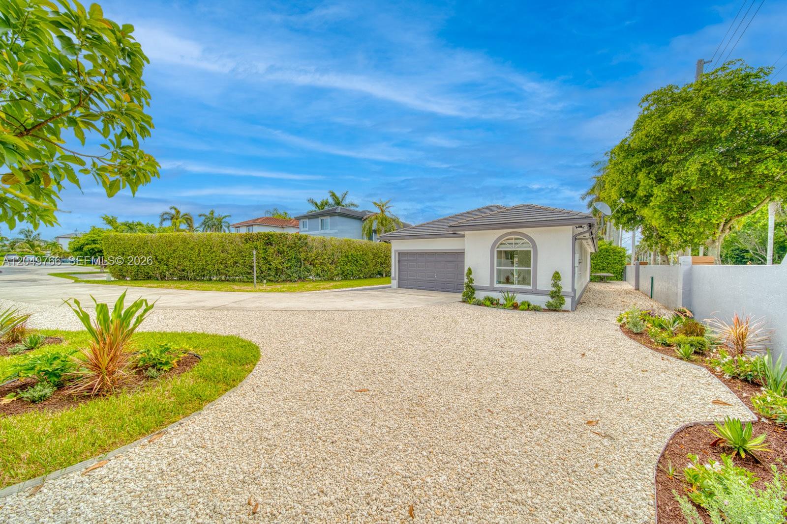 A single-story house with a gray garage and gravel driveway under a blue sky — 15950 SW 71st Ter, Miami FL 33193, MIAMI, FL