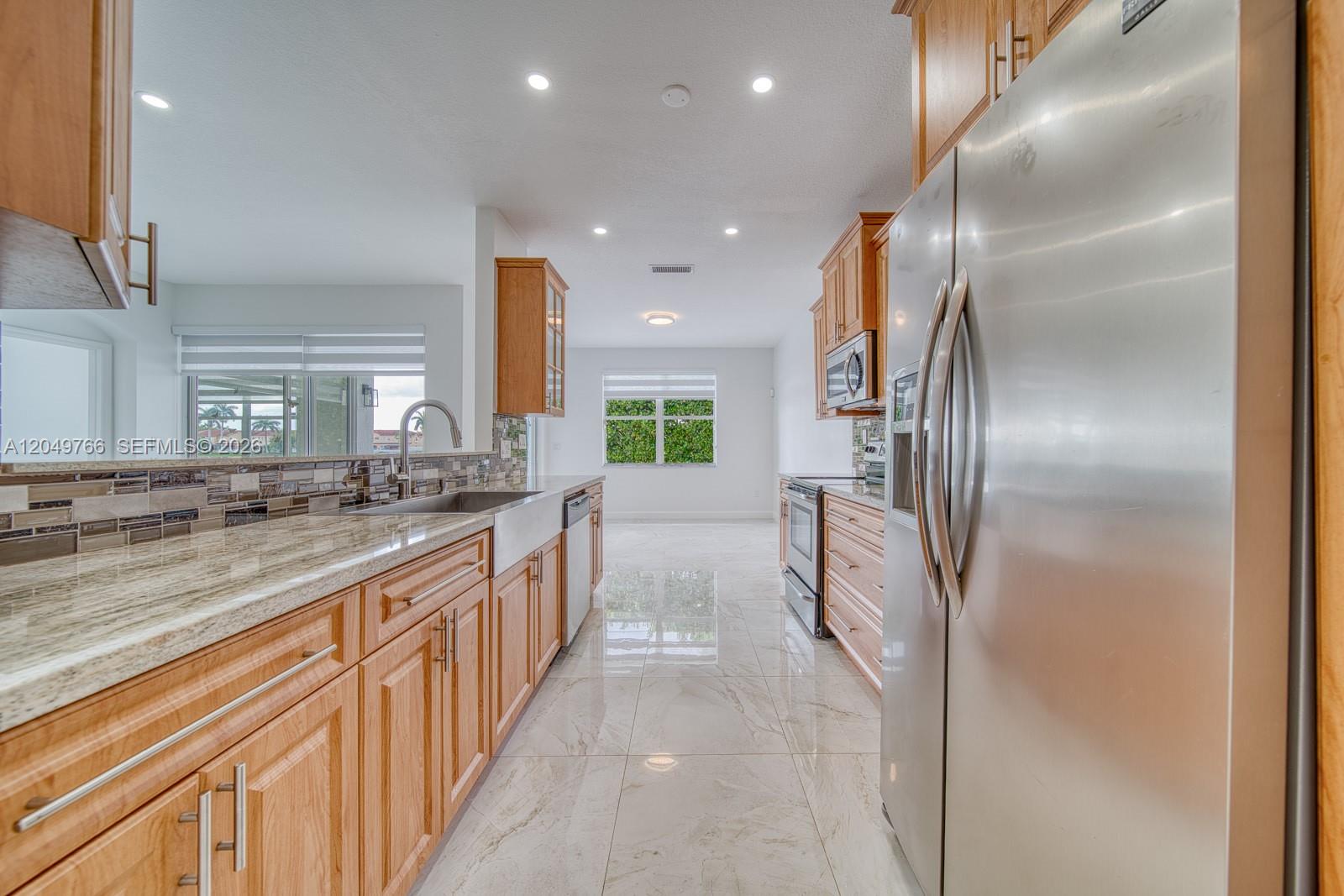 A kitchen features light wood cabinets, granite countertops, stainless steel appliances, and polished tile floors — 15950 SW 71st Ter, Miami FL 33193, MIAMI, FL