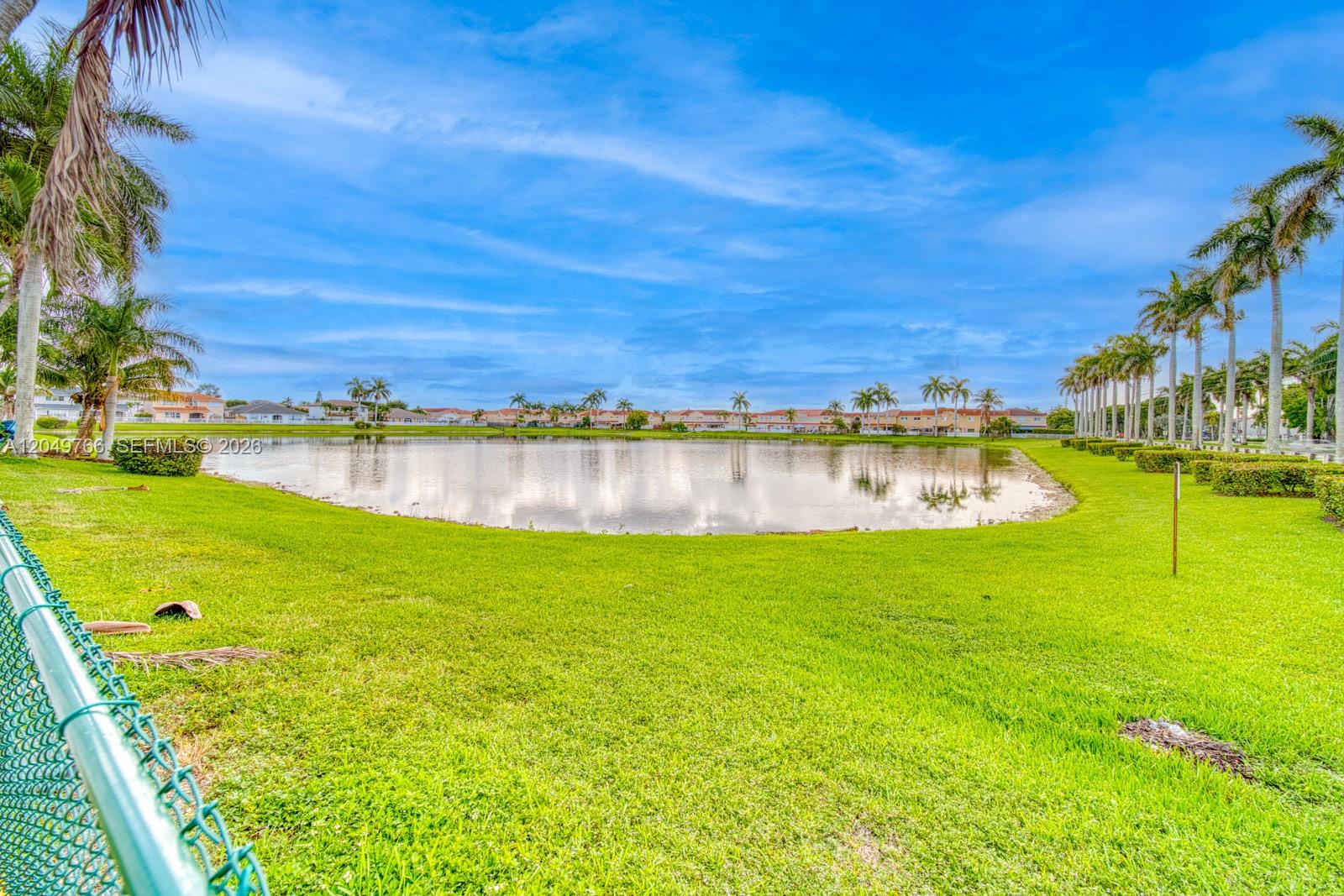 A grassy lawn leads to a pond surrounded by palm trees and residential buildings — 15950 SW 71st Ter, Miami FL 33193, MIAMI, FL