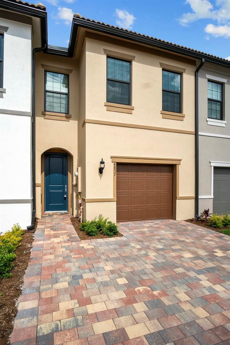A two-story townhouse exterior features a tan stucco facade, brown garage door, and paver driveway — 4837 Chantilly Road, Lake Worth FL 33467, LAKE WORTH, FL