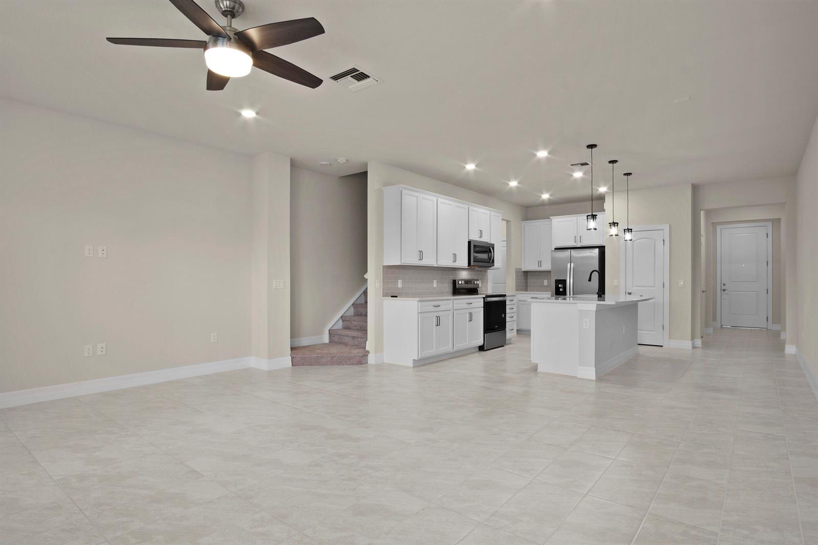 An open-concept kitchen and living area features white cabinets, stainless appliances, and tile flooring — 4837 Chantilly Road, Lake Worth FL 33467, LAKE WORTH, FL