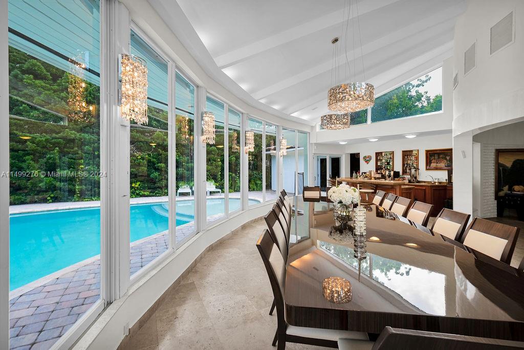 A dining room with a large table, crystal chandeliers, and floor-to-ceiling windows overlooking a pool — 61 Camden Ct, Bal Harbour FL 33154, BAL HARBOUR, FL