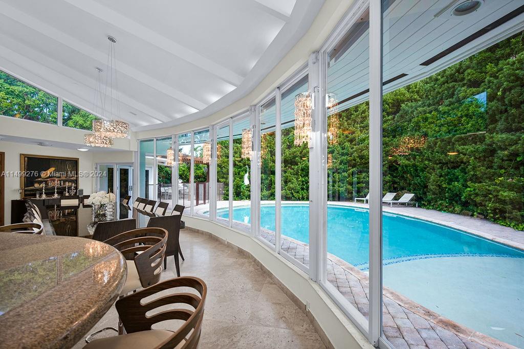 A sunroom with tile floors and glass walls overlooks a swimming pool and lush greenery — 61 Camden Ct, Bal Harbour FL 33154, BAL HARBOUR, FL
