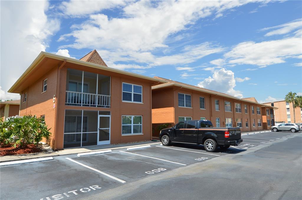 A multi-story apartment building with screened balconies and a parking lot in the foreground — 12760 INDIAN ROCKS ROAD UNIT 605, LARGO, FL