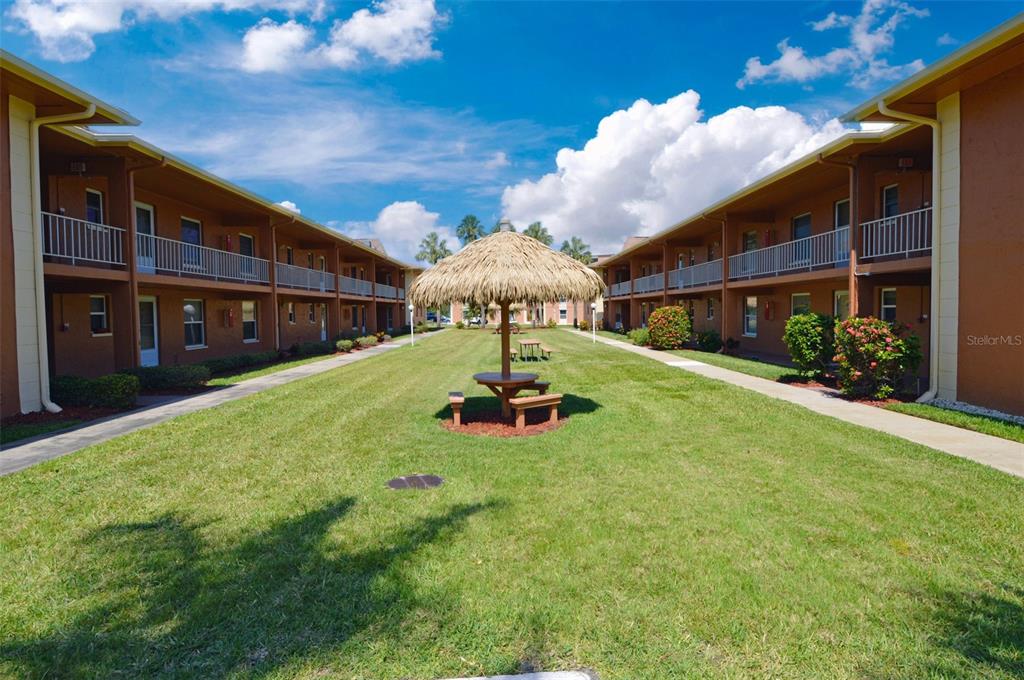 A grassy courtyard sits between two two-story apartment buildings with a tiki-style picnic table — 12760 INDIAN ROCKS ROAD UNIT 605, LARGO, FL