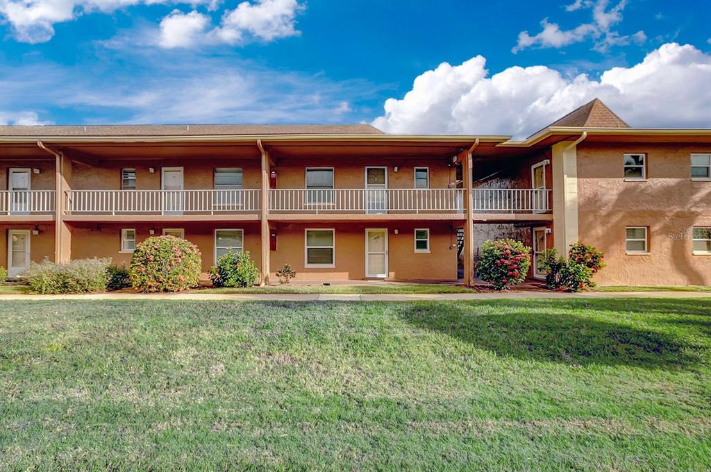 A two-story apartment building with tan stucco walls, white railings, and a grassy lawn — 12760 INDIAN ROCKS ROAD UNIT 605, LARGO, FL