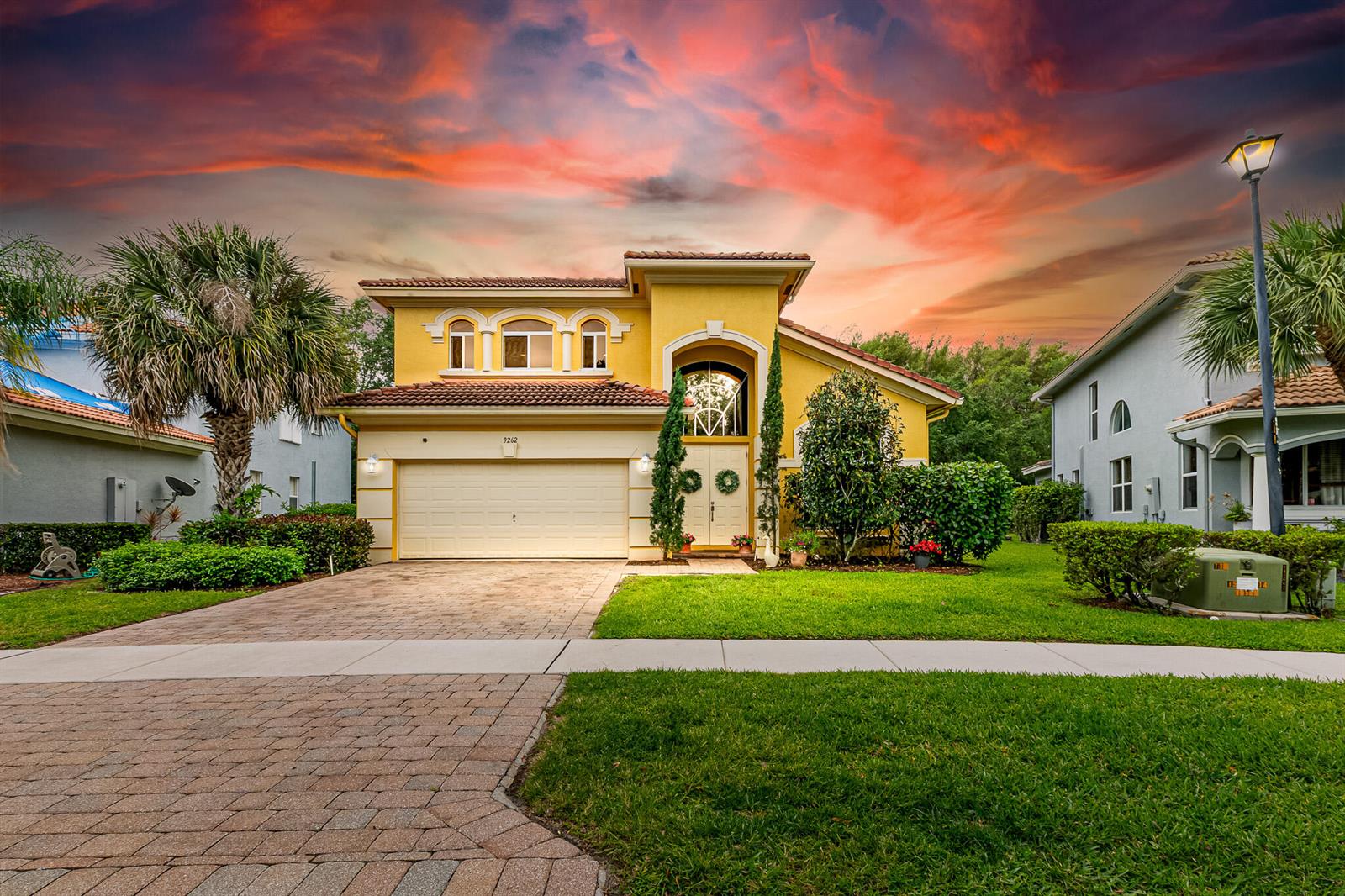 A yellow two-story house with a tile roof and a paved driveway at sunset — 9262 Silver Glen Way, Lake Worth FL 33467, LAKE WORTH, FL