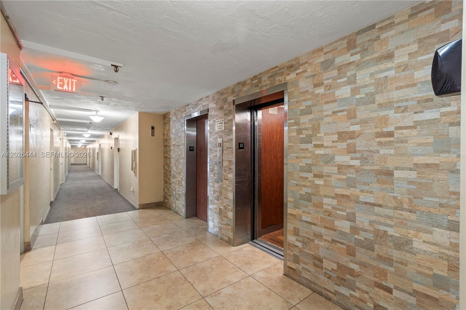 A hallway features two elevators with wood-paneled doors and a stone-tiled accent wall — 7100 NW 17th St # 219, Plantation FL 33313, PLANTATION, FL