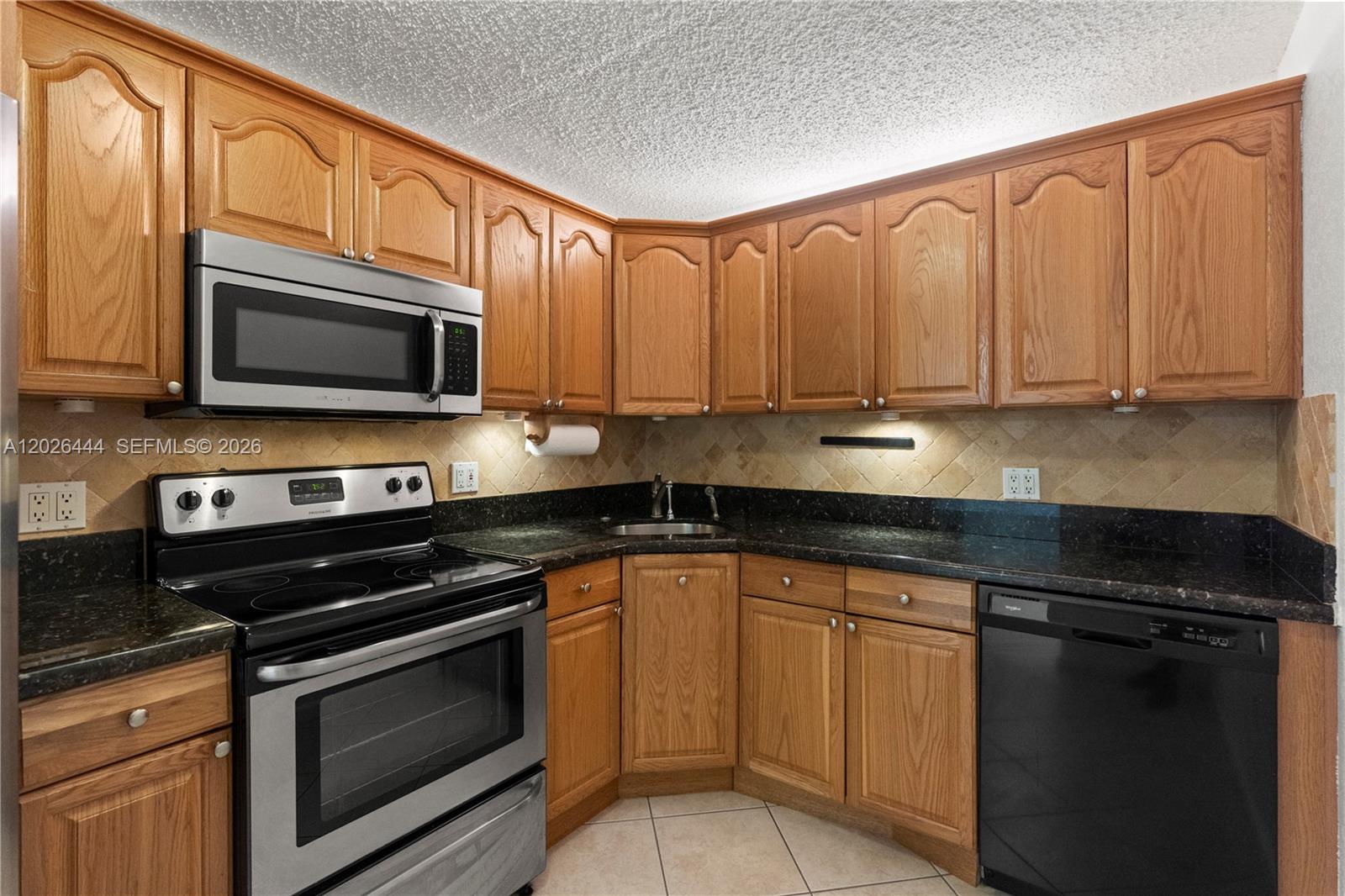 A kitchen features oak cabinets, black countertops, stainless steel appliances, and a tiled backsplash — 7100 NW 17th St # 219, Plantation FL 33313, PLANTATION, FL
