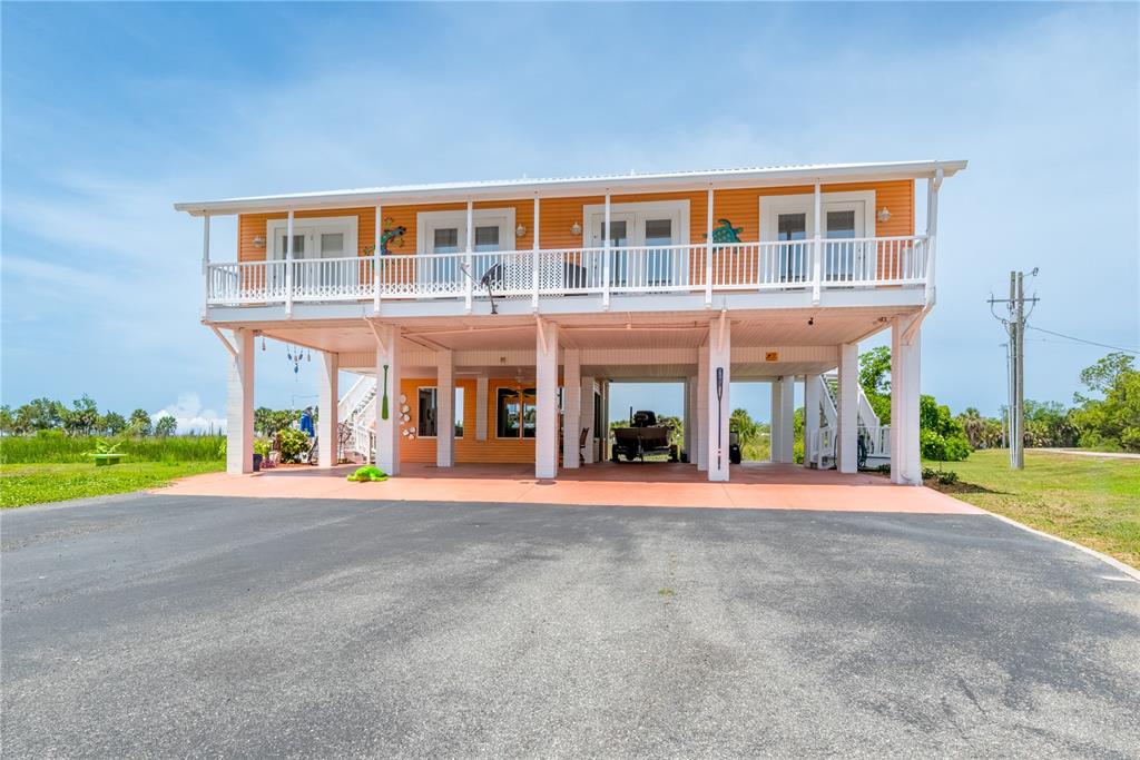 An elevated orange house with a large deck stands above a paved parking area — 200/202 NE 205TH STREET, SUWANNEE, FL