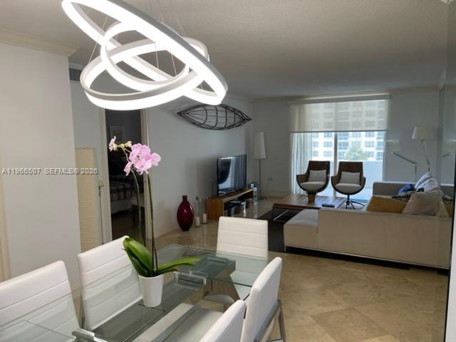 A dining area with a modern chandelier overlooks a living room with tile flooring — 5555 Collins Ave # 7Z, Miami Beach FL 33140, MIAMI BEACH, FL