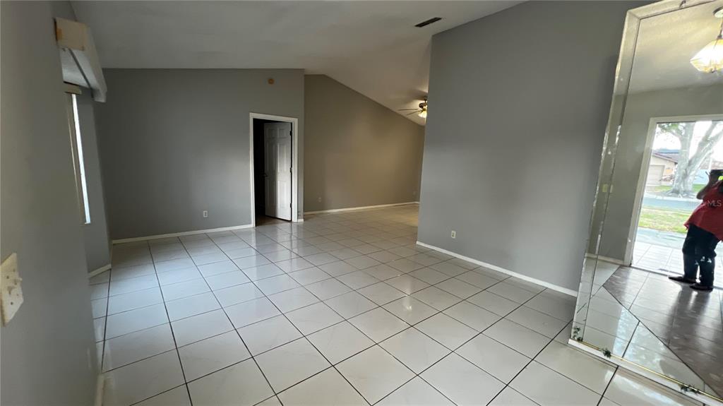 A living area with light gray walls, white tiled floors, and a vaulted ceiling — 6409 ROYAL TERN STREET, ORLANDO, FL