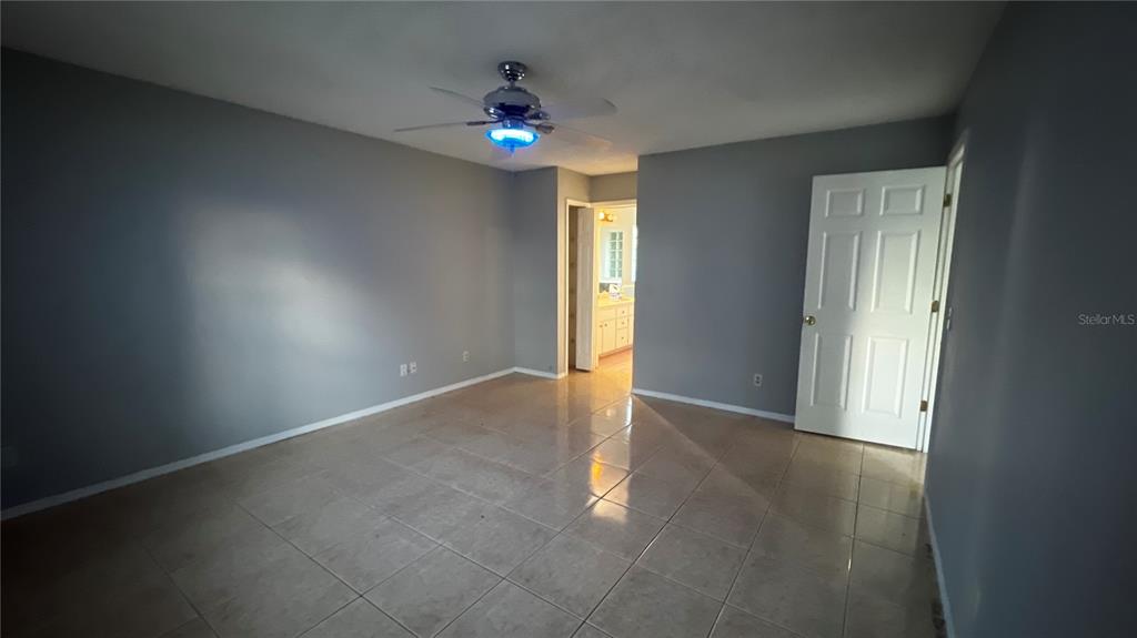 An empty bedroom features gray walls, a tiled floor, and a ceiling fan with blue lighting — 6409 ROYAL TERN STREET, ORLANDO, FL