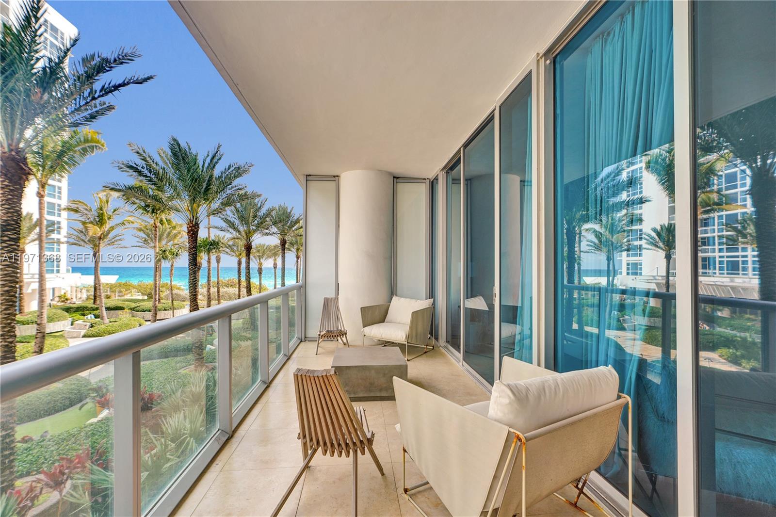 A balcony with outdoor furniture overlooks a tropical landscape and the ocean — 6799 Collins Ave # 201, Miami Beach FL 33141, MIAMI BEACH, FL