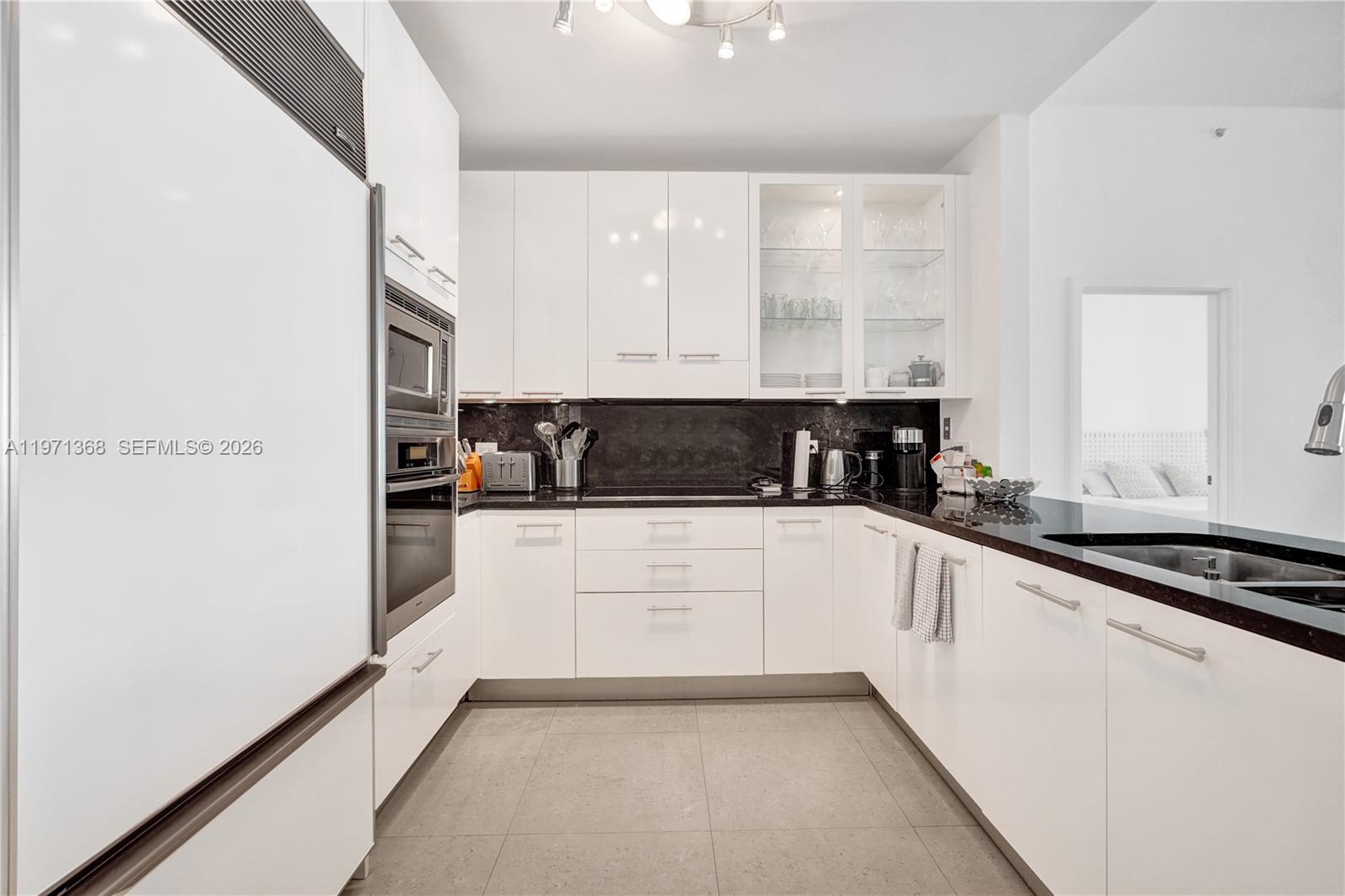 A modern kitchen features white cabinets, black countertops, and stainless steel appliances — 6799 Collins Ave # 201, Miami Beach FL 33141, MIAMI BEACH, FL