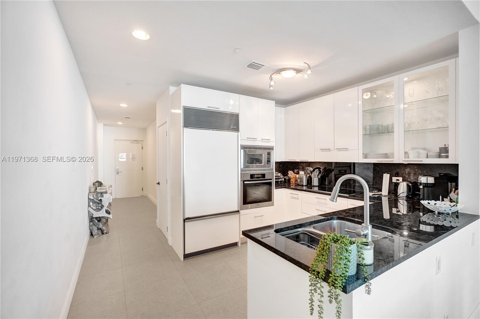A modern kitchen features white cabinetry, black granite countertops, and stainless steel appliances — 6799 Collins Ave # 201, Miami Beach FL 33141, MIAMI BEACH, FL