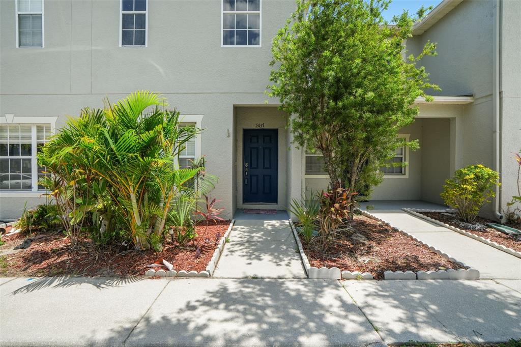 A two-story townhouse exterior features a dark blue front door and landscaped garden beds — 13137 KINGS CROSSING DRIVE, GIBSONTON, FL