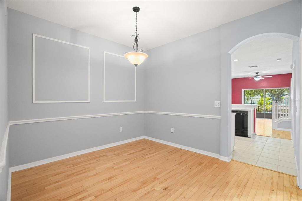 A dining room with light gray walls, white wainscoting, hardwood floors, and a hanging light fixture — 13137 KINGS CROSSING DRIVE, GIBSONTON, FL