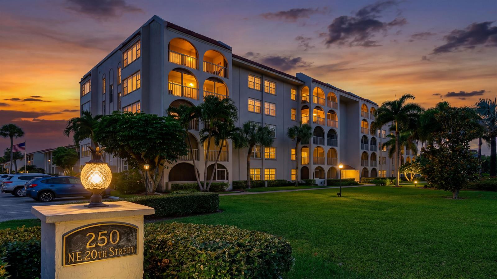 A multi-story apartment building with arched balconies stands on a grassy lawn at sunset — 250 NE 20th Street # 5260, Boca Raton FL 33431, BOCA RATON, FL