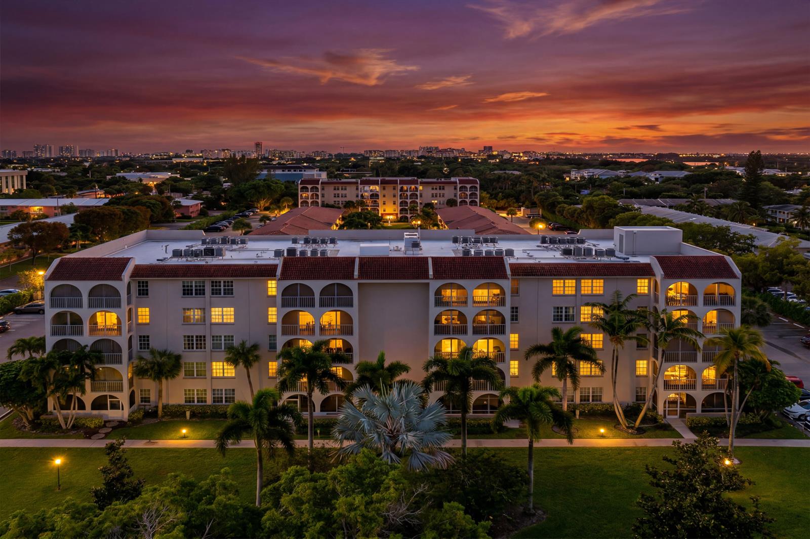 An aerial view of a multi-story apartment building at sunset with palm trees and landscaping — 250 NE 20th Street # 5260, Boca Raton FL 33431, BOCA RATON, FL