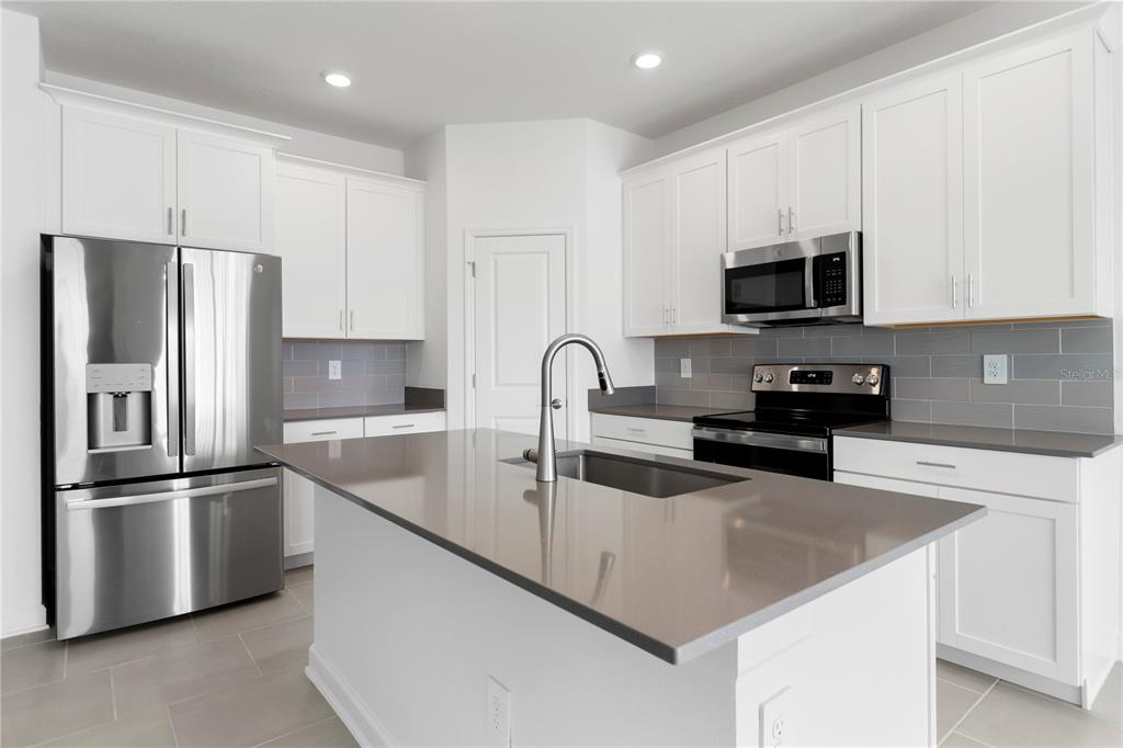 A modern kitchen features white cabinets, stainless steel appliances, and a central island with countertops — 5786 STEPHENS ROAD, ST CLOUD, FL