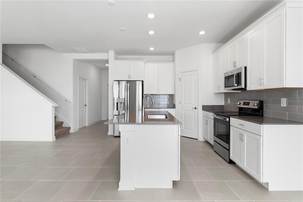A modern kitchen features white cabinets, stainless steel appliances, a center island, and tile flooring — 5786 STEPHENS ROAD, ST CLOUD, FL