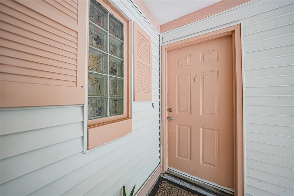 A peach-colored front door sits beside a window with glass blocks and pink shutters — 1051 FORREST NELSON BOULEVARD UNIT 201, PORT CHARLOTTE, FL