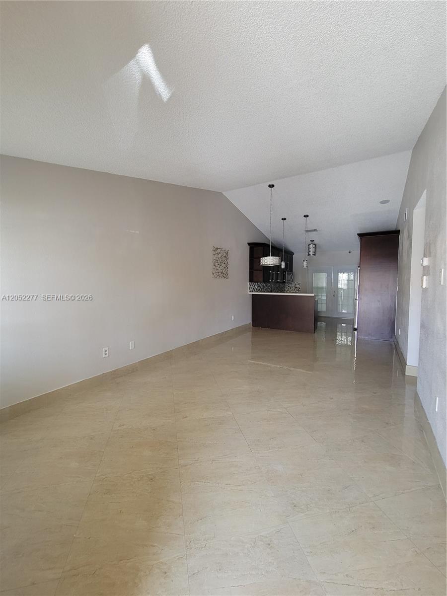An open-concept living area features light-colored tile flooring, beige walls, and a kitchen with dark cabinetry — 7191 W 24th Ave, Hialeah FL 33016, HIALEAH, FL