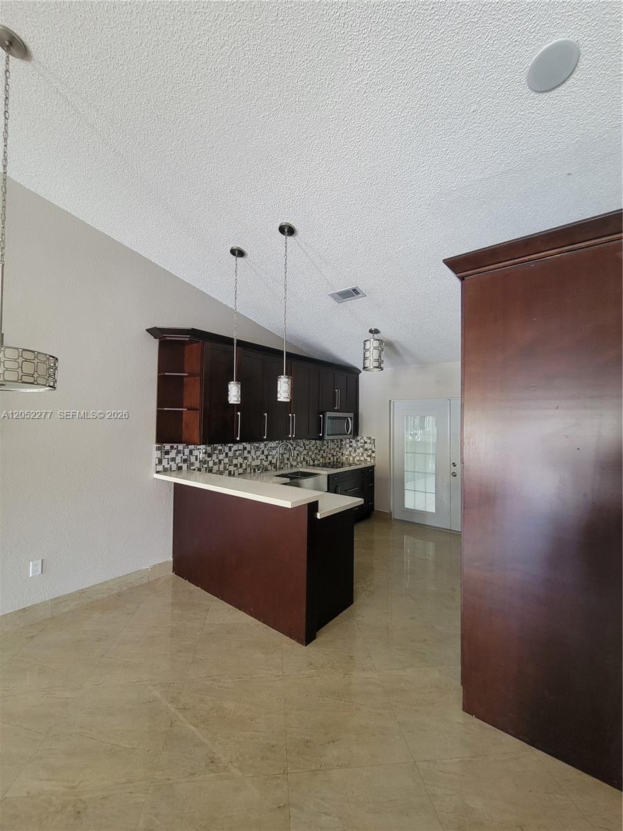 A kitchen features dark wood cabinets, a breakfast bar, and light-colored tile flooring — 7191 W 24th Ave, Hialeah FL 33016, HIALEAH, FL