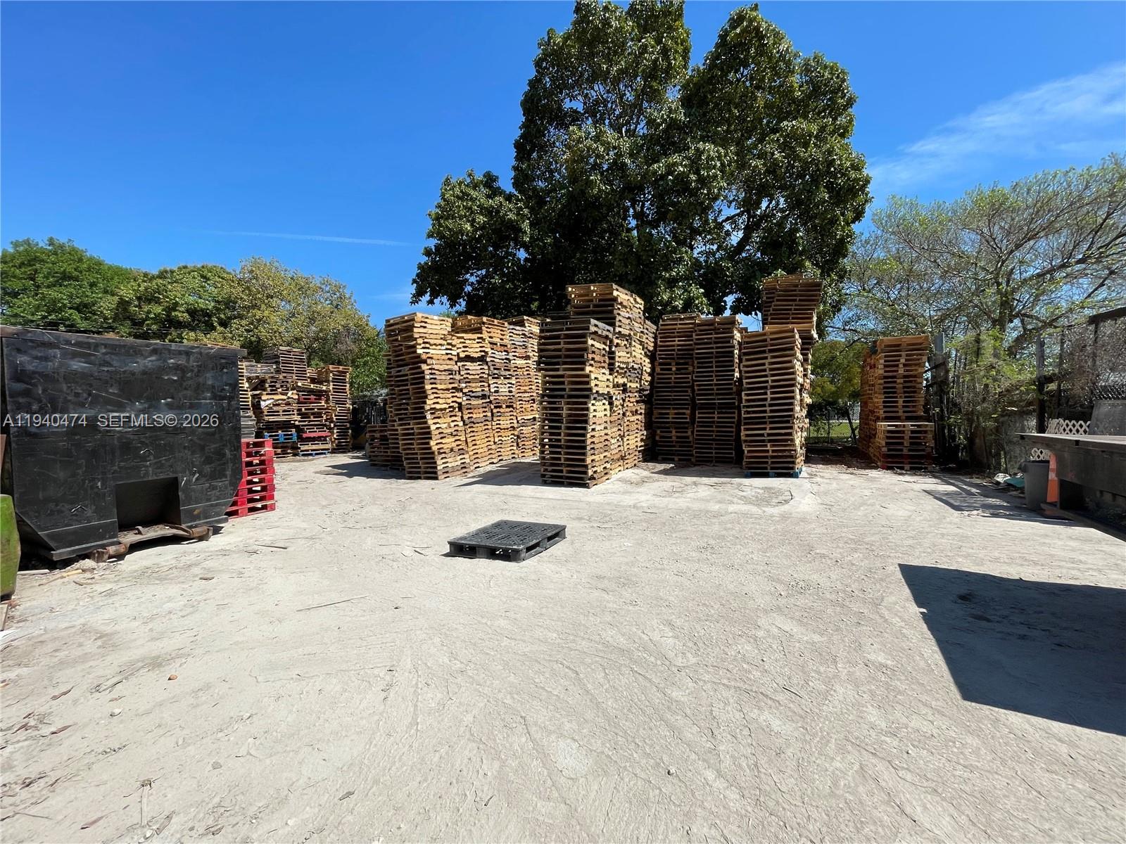 An outdoor storage yard features multiple tall stacks of wooden pallets on concrete ground — 3021 NW 54th St, Miami FL 33142, MIAMI, FL