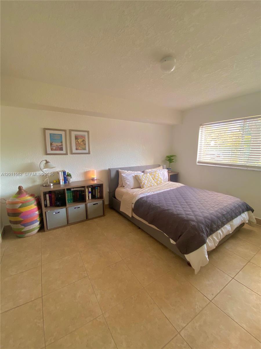 A bedroom features a bed with a gray quilt, a bookshelf, and tile flooring — 445 SW 11th St # 107, Miami FL 33130, MIAMI, FL