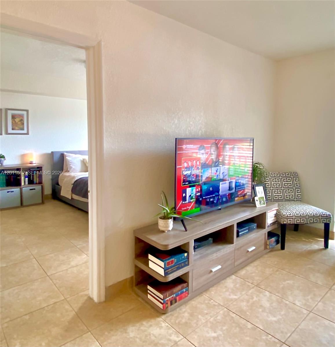 A living area with a television on a wooden stand next to a bedroom doorway — 445 SW 11th St # 107, Miami FL 33130, MIAMI, FL
