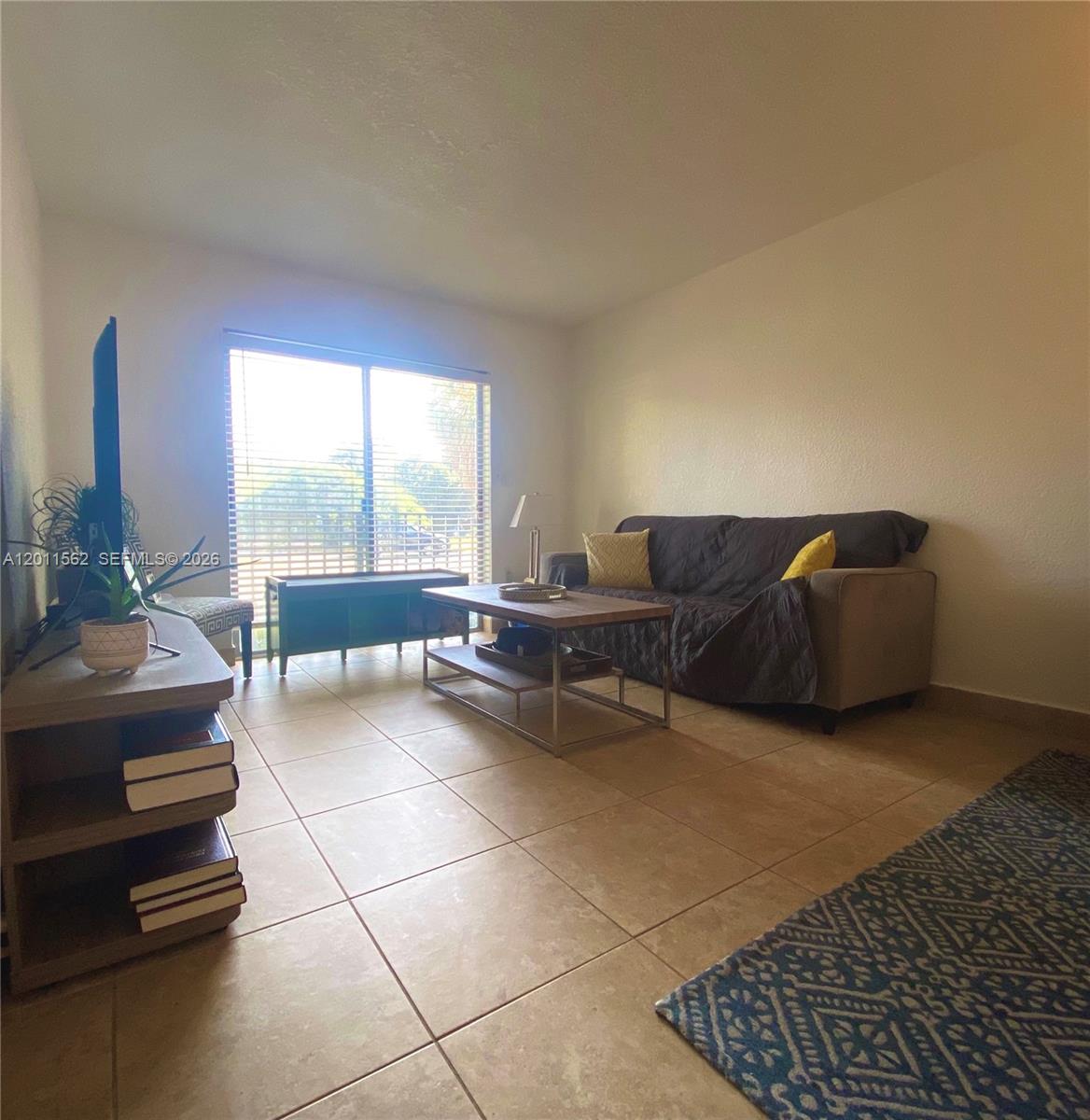 A living room features tile flooring, a sofa, a coffee table, and a sliding glass door — 445 SW 11th St # 107, Miami FL 33130, MIAMI, FL