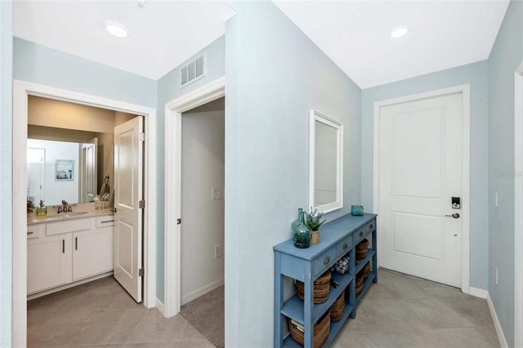 A hallway features light blue walls, tile flooring, a blue console table, and a bathroom entrance — 17655 OPAL SAND DRIVE UNIT 203, VENICE, FL