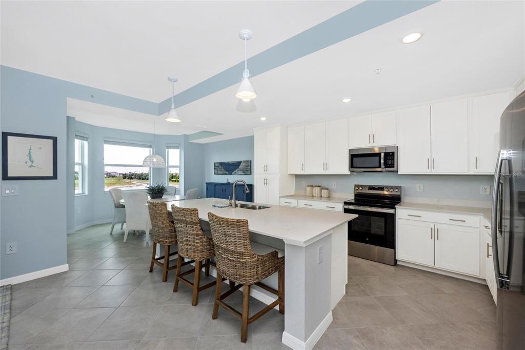 A kitchen with white cabinets, a large island with wicker stools, and light blue walls — 17655 OPAL SAND DRIVE UNIT 203, VENICE, FL