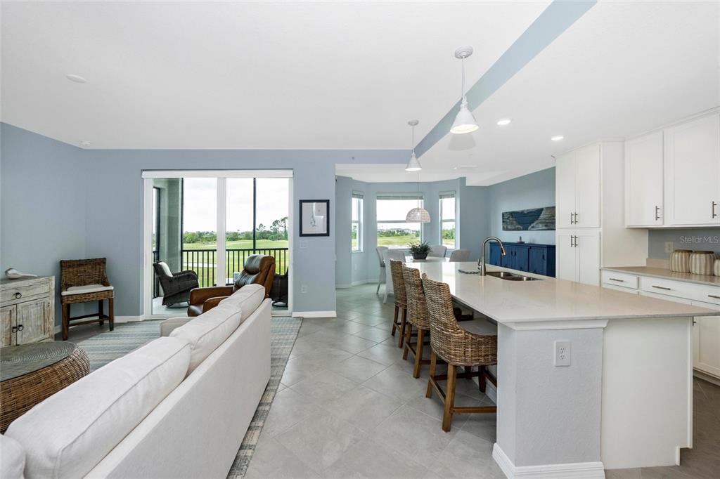 An open-concept kitchen and living area features a large island, tile flooring, and balcony access — 17655 OPAL SAND DRIVE UNIT 203, VENICE, FL