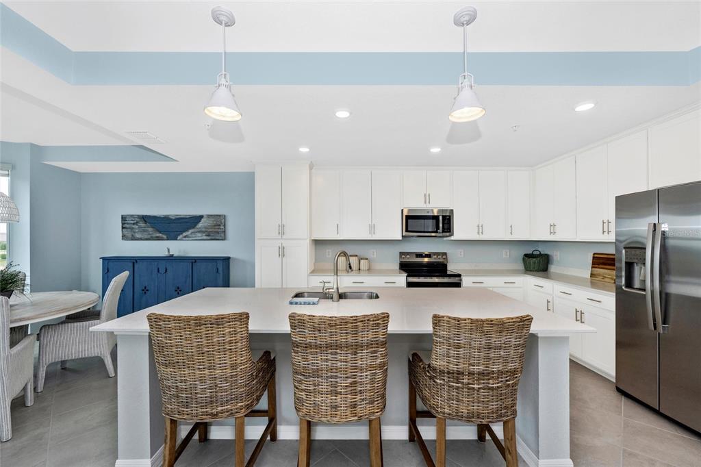 A kitchen features a large island with three wicker stools, white cabinetry, and stainless appliances — 17655 OPAL SAND DRIVE UNIT 203, VENICE, FL