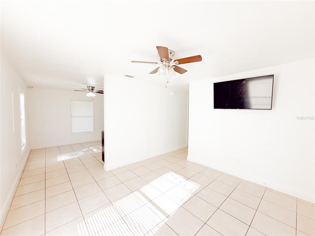 A bright living area features white walls, tile flooring, a ceiling fan, and a wall-mounted television — 407 W BELLA VISTA STREET, LAKELAND, FL