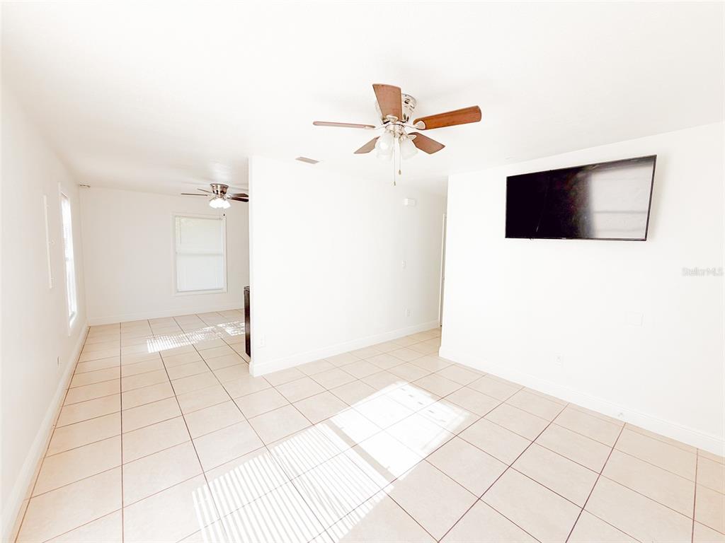 A bright room with white walls, tiled floors, two ceiling fans, and a wall-mounted television — 407 W BELLA VISTA STREET, LAKELAND, FL