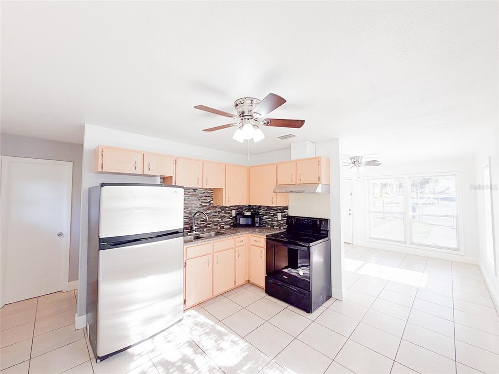 A kitchen with light wood cabinets, stainless steel refrigerator, black stove, and tiled flooring — 407 W BELLA VISTA STREET, LAKELAND, FL