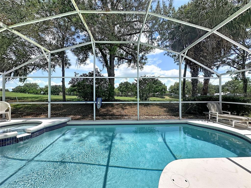 A screened-in swimming pool and spa overlook a grassy yard with mature trees — 2223 MALLORY CIRCLE, HAINES CITY, FL