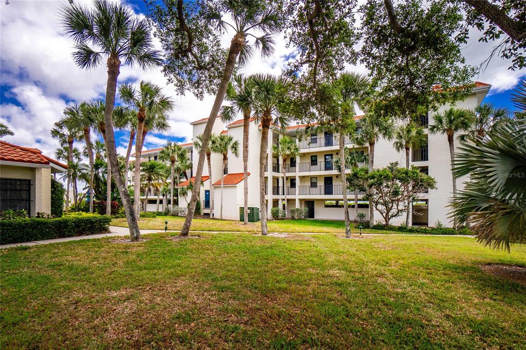 A multi-story apartment building exterior surrounded by palm trees and a grassy lawn — 1591 BEACH ROAD UNIT 407, ENGLEWOOD, FL