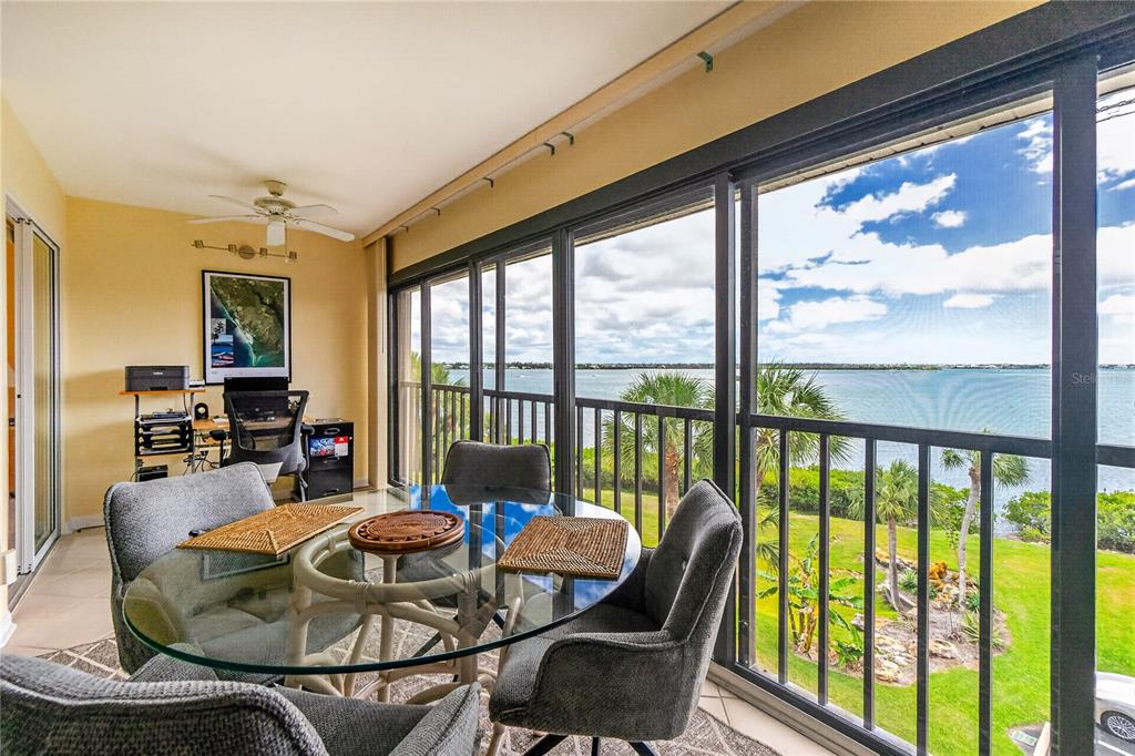 A sunroom with a glass dining table, office area, and large windows overlooking the water — 1591 BEACH ROAD UNIT 407, ENGLEWOOD, FL
