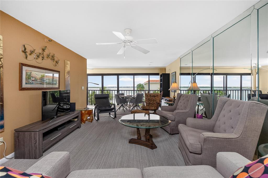 A living room features gray carpeting, a mirrored wall, and a balcony overlooking the water — 1591 BEACH ROAD UNIT 407, ENGLEWOOD, FL