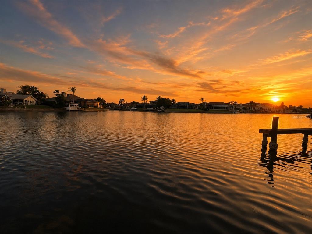 A sunset view over a calm canal with houses and a wooden dock in the foreground — 4804 LONGWATER WAY, TAMPA, FL