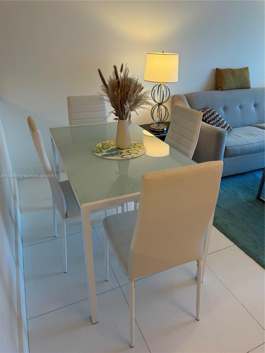 A dining area features a glass-topped table with four white chairs and a table lamp — 6801 Collins Ave # C1115, Miami Beach FL 33141, MIAMI BEACH, FL