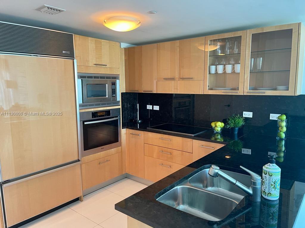 A kitchen features light wood cabinets, black countertops, stainless steel appliances, and a double sink — 6801 Collins Ave # C1115, Miami Beach FL 33141, MIAMI BEACH, FL