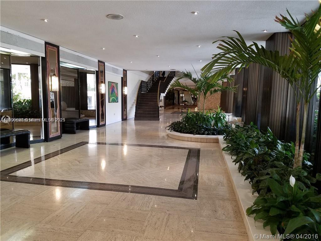 A spacious lobby features marble floors, a central staircase, and indoor planters with palm trees — 5555 Collins Ave # 11U, Miami Beach FL 33140, MIAMI BEACH, FL