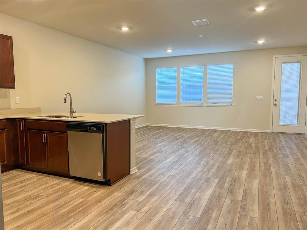 A kitchen with dark wood cabinets and a stainless dishwasher opens into a living area — 10363 FOLLY BEACH ROAD, ORLANDO, FL