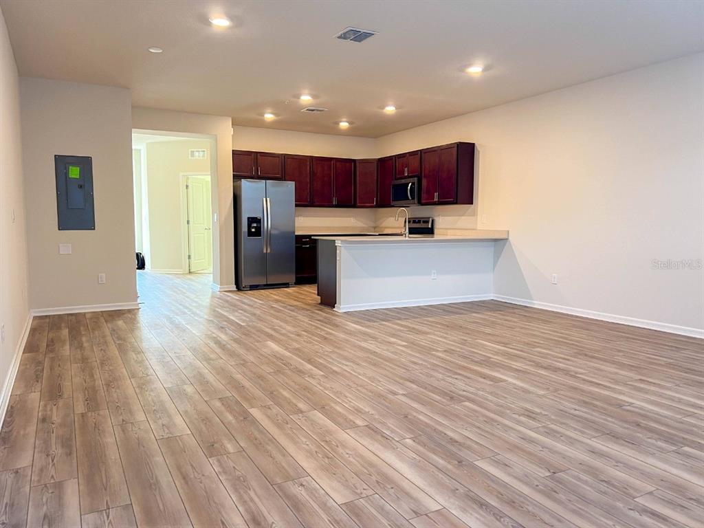 An open-concept kitchen features dark wood cabinets, stainless steel appliances, and light wood-look flooring — 10363 FOLLY BEACH ROAD, ORLANDO, FL